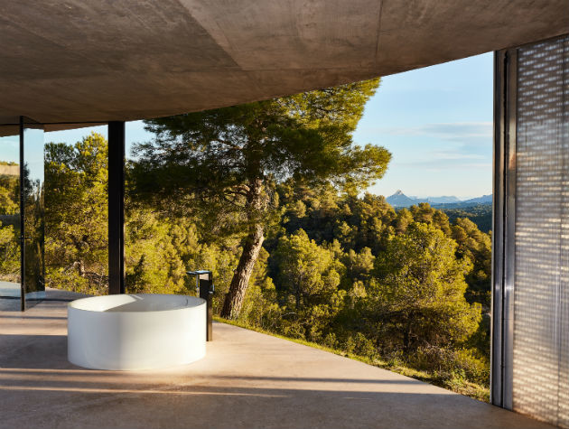 A circular freestanding bath next to an open window overlooking trees